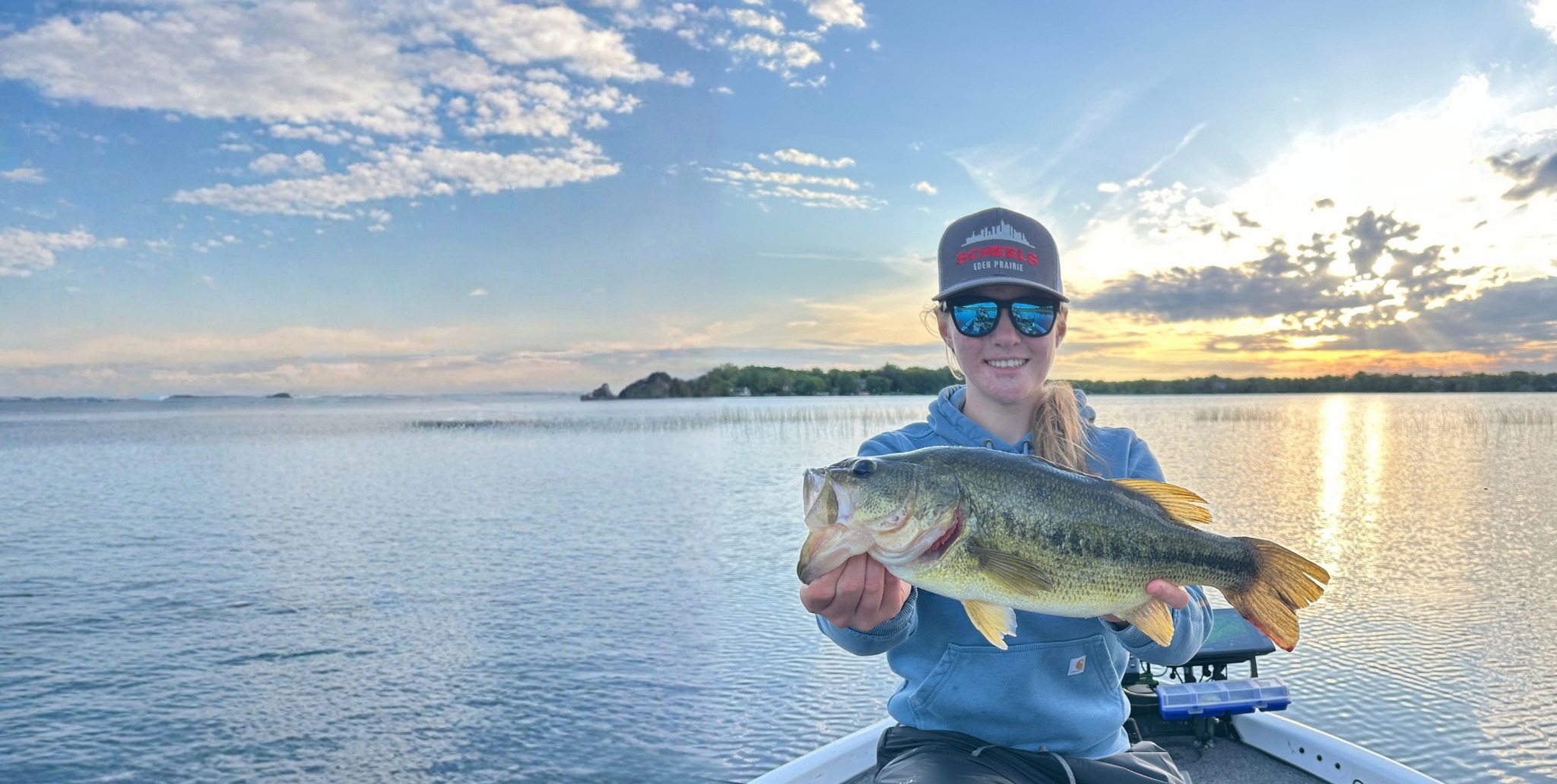 Student angler holding a bass on the water at sunset