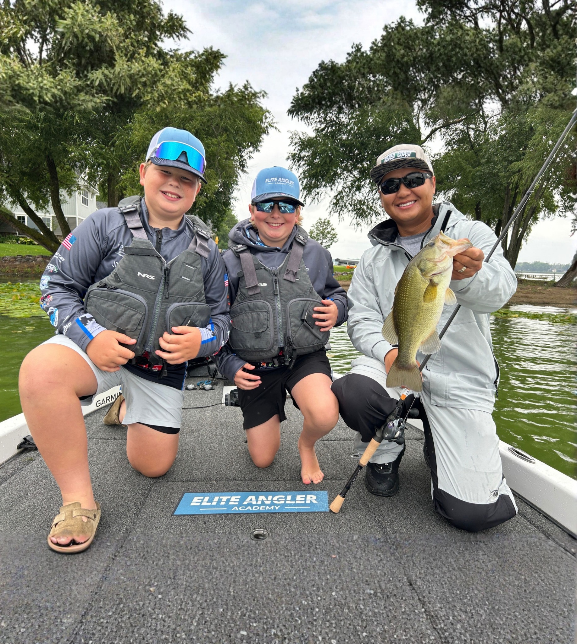 Trevor Lo holding a bass alongside two student anglers in the boat